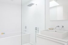 a white minimalist bathroom with a skylight, a white floating vanity, white appliances and built-in lights