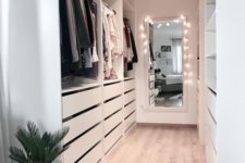 a white minimalist closet with drawers, open shelving and holders plus a mirror with lights to see what to wear