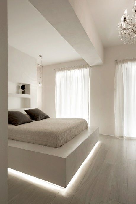a white ultra-minimalist bedroom with a floating slab bed with lighting, niches for storage, a crystal chandelier for an elegant touch