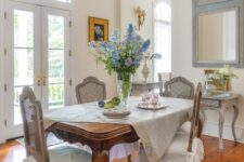 an exquisite French chic dining room with a stained vintage table, grey vintage chairs, a mirror, a whitewashed console table and a vintage chandelier