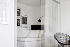 a Nordic bedroom with a bed and some black and white artworks separated from the rest of the apartment with a glass sliding door