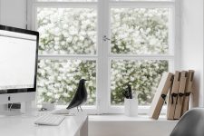 a Scandinavian home office with a window to the blooming garden, a white desk, a black chair is a pretty and cool space to work in