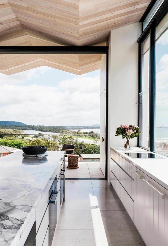a beautiful light-filled contemporary kitchen with neutral cabinets, a kitchen island with a marble countertop and a glazed wall that can be removed