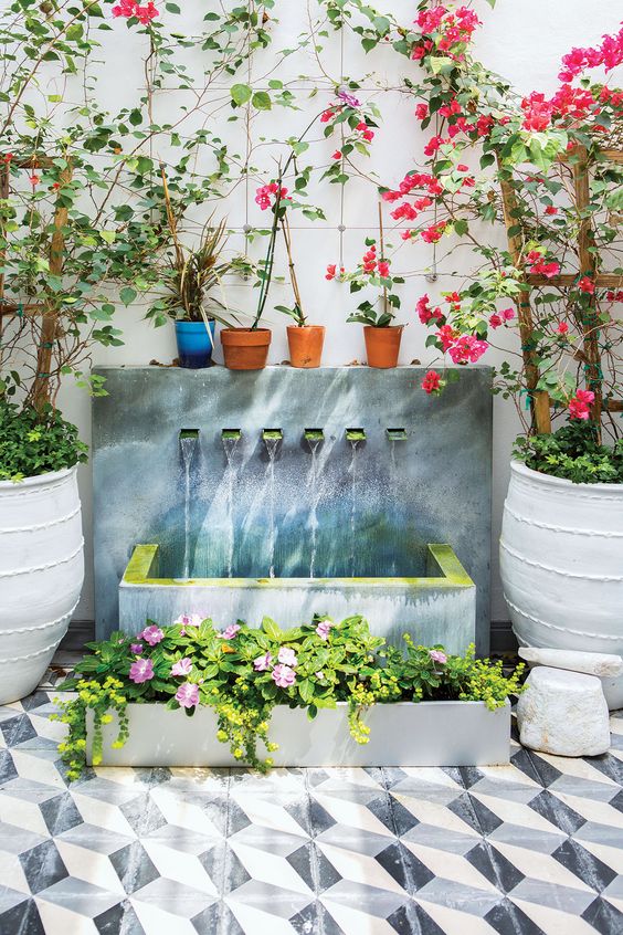 une belle fontaine murale moderne avec plusieurs robinets, une baignoire en béton et une jardinière assortie avec des fleurs à côté une belle fontaine murale moderne avec plusieurs robinets, une baignoire en béton et une jardinière assortie avec des fleurs à côté