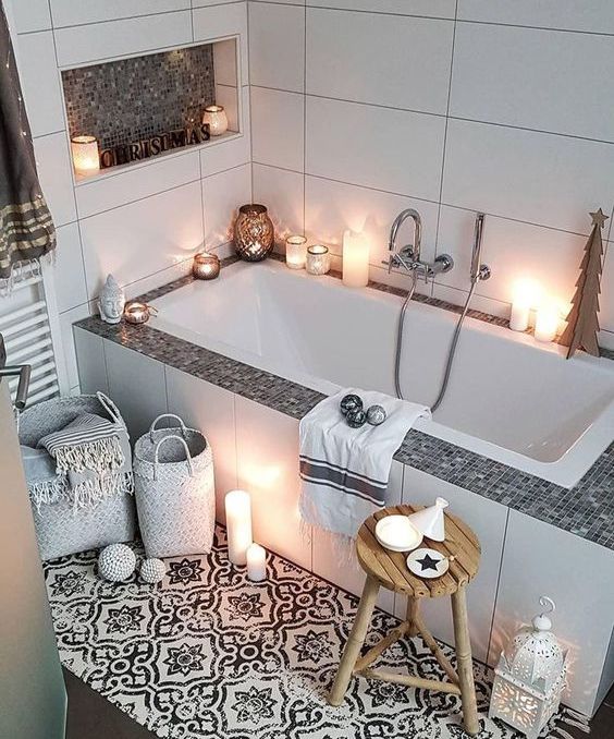 a beautiful monochromatic mini home space wiht large scale white and printed tiles, a tub surrounded with tiles, candles, candle lanterns and a niche for storage