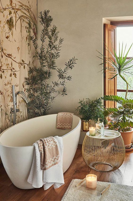 a botanical inspired spa bathroom with an accent wall, an oval tub, lots of potted plants, an elegant round side table and candles