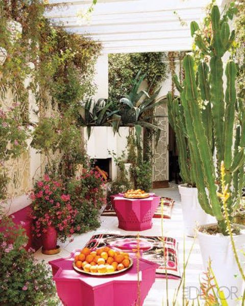 a bright and chic terrace with a fireplace, pink coffee tables, bold blooms and greenery, printed cushions on the floor