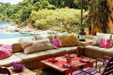 a bright and colorful terrace with neutral upholstered benches, colorful pillows, bright stools and textiles plus a sea view
