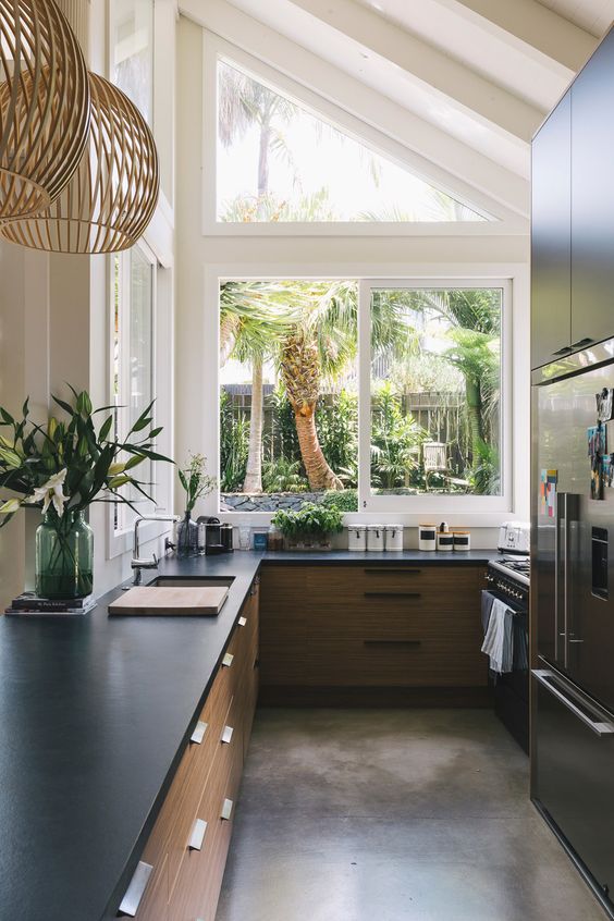 a chic modern kitchen with light-stained cabinets, black stone countertops, a large attic window with a tropical garden view