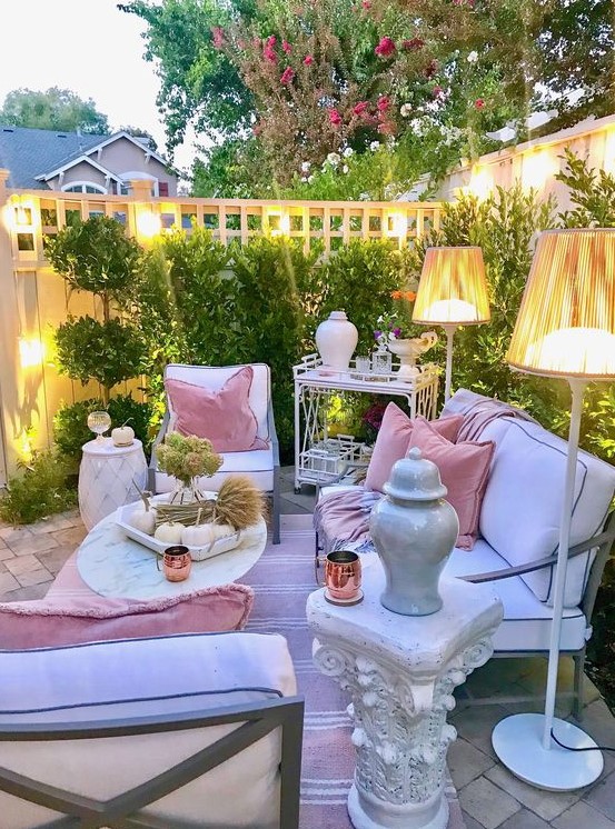 a chic pastel terrace with white contemporary furniture, floor lamps, refined tables and a greenery wall
