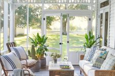 a coastal screened porch with wicker furniture, a stained coffee table, potted plants and bright pillows
