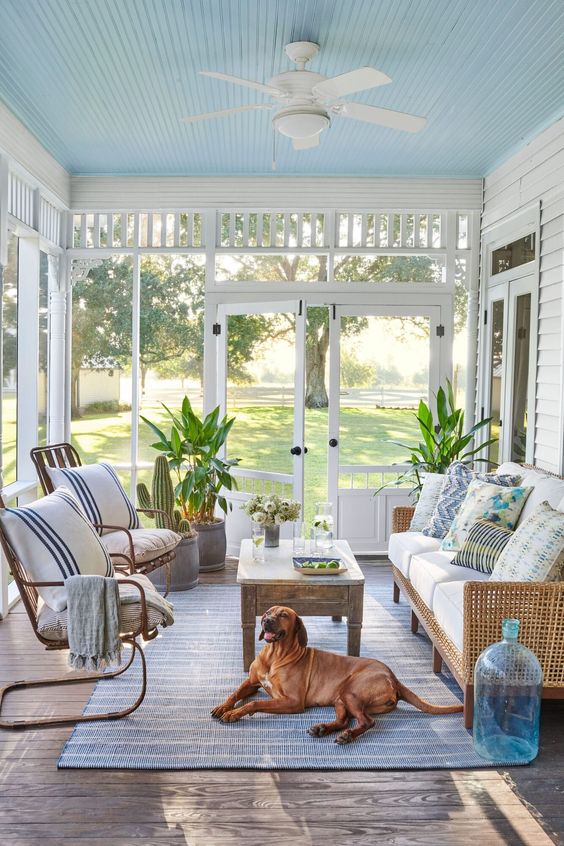 a coastal screened porch with wicker furniture, a stained coffee table, potted plants and bright pillows