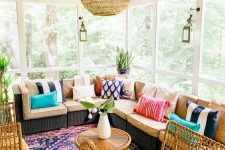 a colorful boho screened porch with a corner wicker sofa with colorful pillows, rattan chairs and a bold printed rug