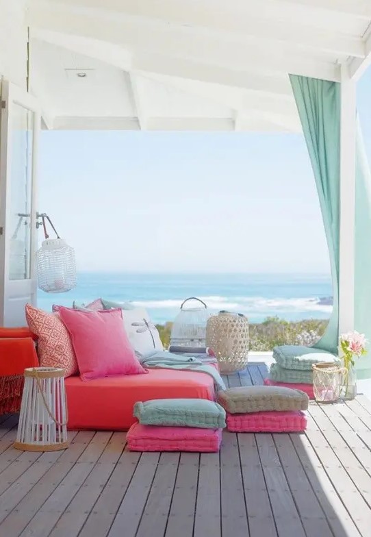 a colorful summer seaside terrace with a bright daybed, colorful pillows and cushions and candle lanterns
