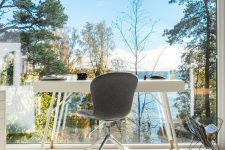 a contemporary home office with a glazed wall and a forest and lake view, a white desk and a grey chair – everything is done to enjoy the views
