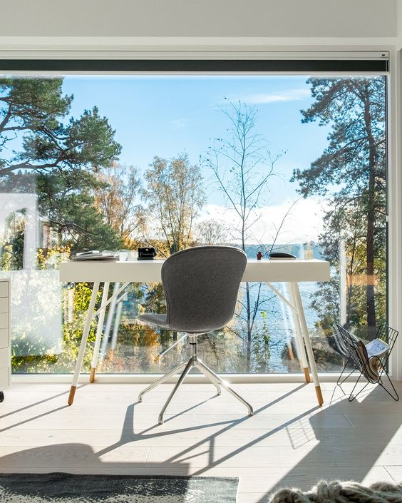 a contemporary home office with a glazed wall and a forest and lake view, a white desk and a grey chair   everything is done to enjoy the views