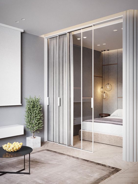 a contemporary neutral bedroom with an upholstered bed, some lights and pendant lamps and curtains over a glass wall that connects it to the rest of the house