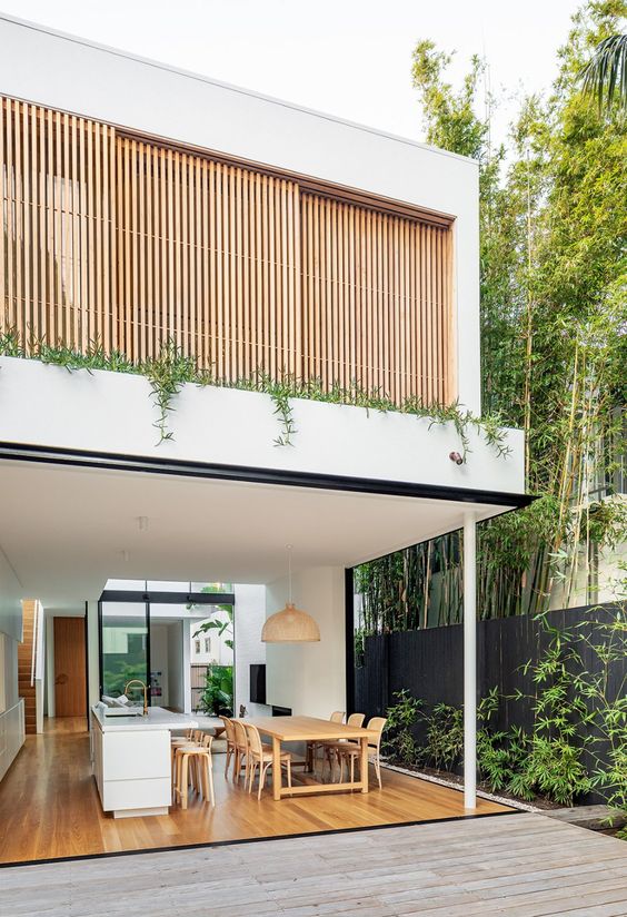 a contemporary white kitchen with a large kitchen island, a dining zone with stained furniture and walls that can be opened to tha garden
