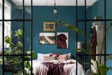 a cozy bedroom with a bed, a vintage storage unit and some bold art, with hunter green walls and a glass wall with doors