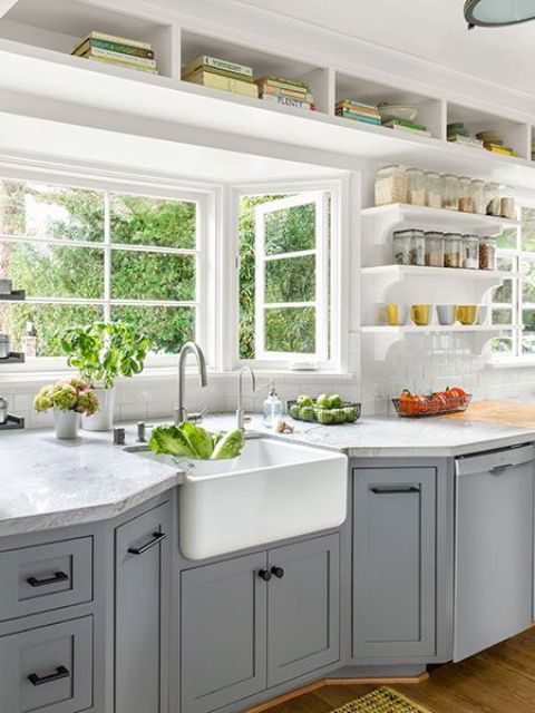 a cozy grey farmhouse kitchen with shaker style cabinets, white stone countertops, built-in shelves and a bay window that opens on the garden