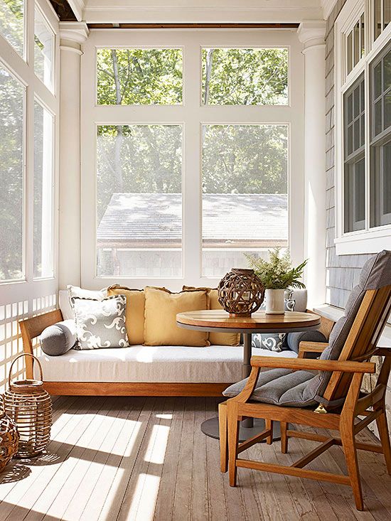 a cozy neutral screened porch with a white daybed with lots of pillows, a stained chair with grey upholstery, greenery and lanterns
