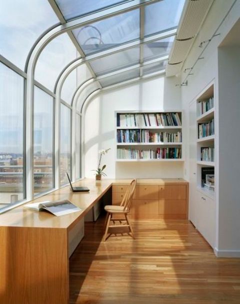a creative sunroom home office with a glazed ceiling and wall with city views, a large built-in desk and lots of built-in bookshelves