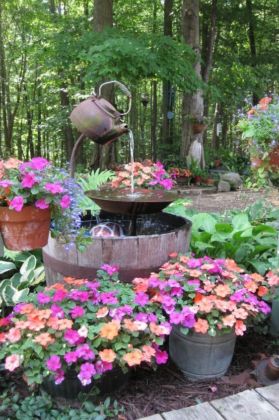 a creative vintage rustic fountain made of a metal teapot and a bowl, some bright blooms and greenery around