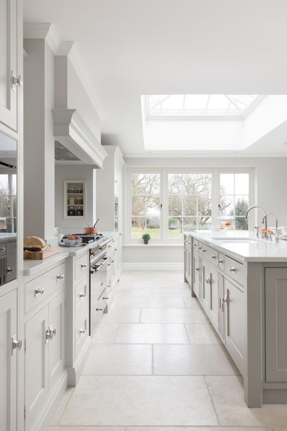 a dove grey kitchen with shaker style cabinets, white stone countertops, a large skylight and windows that open on the garden