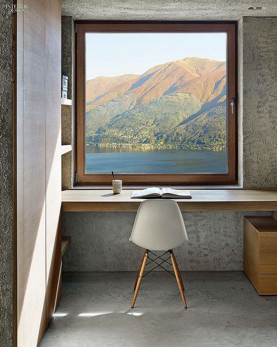 a fantastic home office nook in minimal style, with a window to a lake and mountains, built in shelves and a built in desk, a white chair