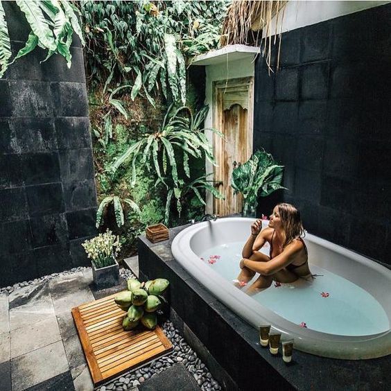 a fully secluded outdoor spa with planted greenery and a living wall, a tub and some tiles plus a wooden mat