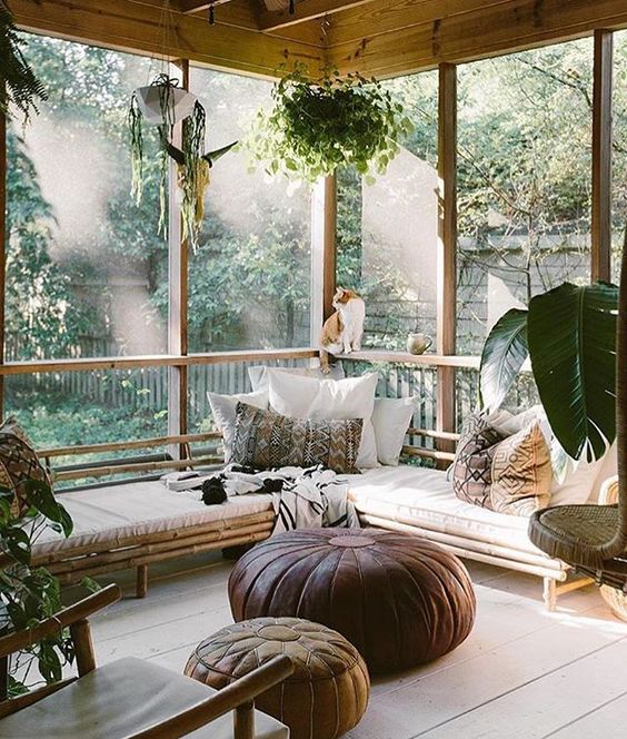 a gorgeous boho screened patio with a corner rattan bench with boho pillows, leather poufs, potted greenery is super welcoming