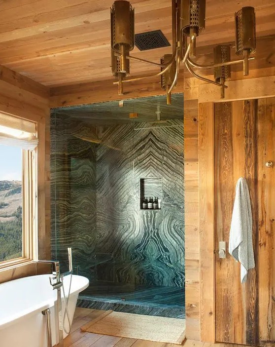 a gorgeous chalet bathroom done with light stained wood and green marble in the shower, a tub with a view