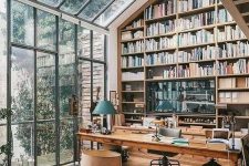 a greenhouse-style home office with an oversized bookcase reaching the roof, a glazed wall and ceiling with garden views and cool vintage and modern furniture