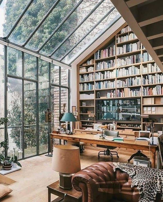 a greenhouse style home office with an oversized bookcase reaching the roof, a glazed wall and ceiling with garden views and cool vintage and modern furniture