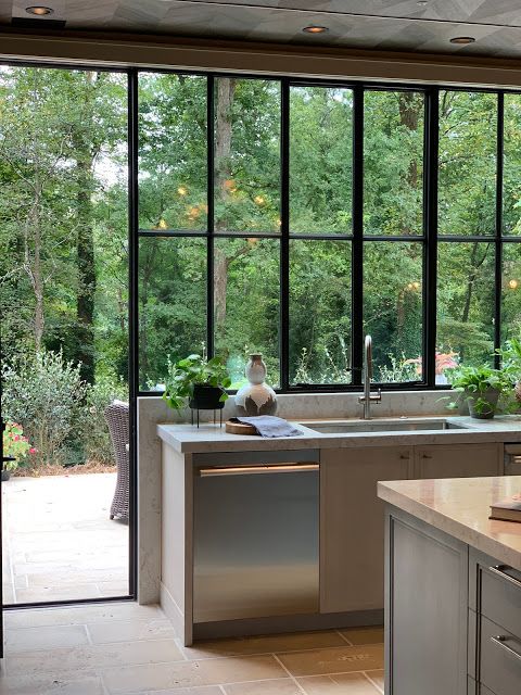 a grey gallery kitchen with neutral stone countertops, a glazed wall with forest views that become part of decor