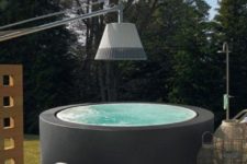 a hot tub clad with a matte black surface, with some candle lanterns and a daybed by its side