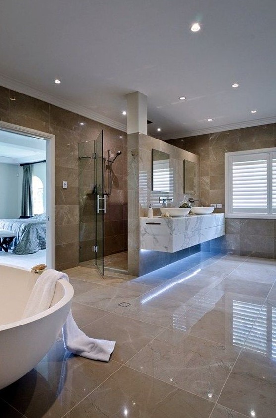 a large luxurious bathroom with tan and brown tiles, built in lights, white appliances and a marble vanity
