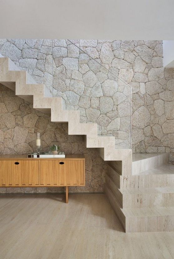 a  limestone statement wall and a matching neutral staircase with clear glass railing for an ultimate contemporary space