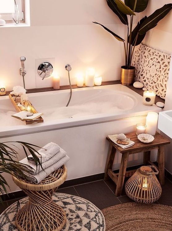 a little home spa bathroom with a tub, candles and pebbles surrounding it, a wooden stool and a candle lantern