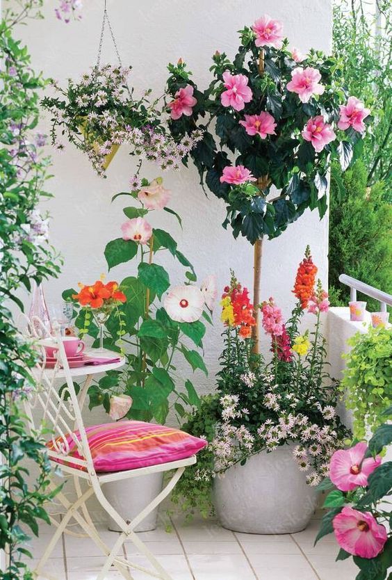 a lovely blacony with white forged furniture, pink cushions, potted blooms of various kinds is a cool feminine space