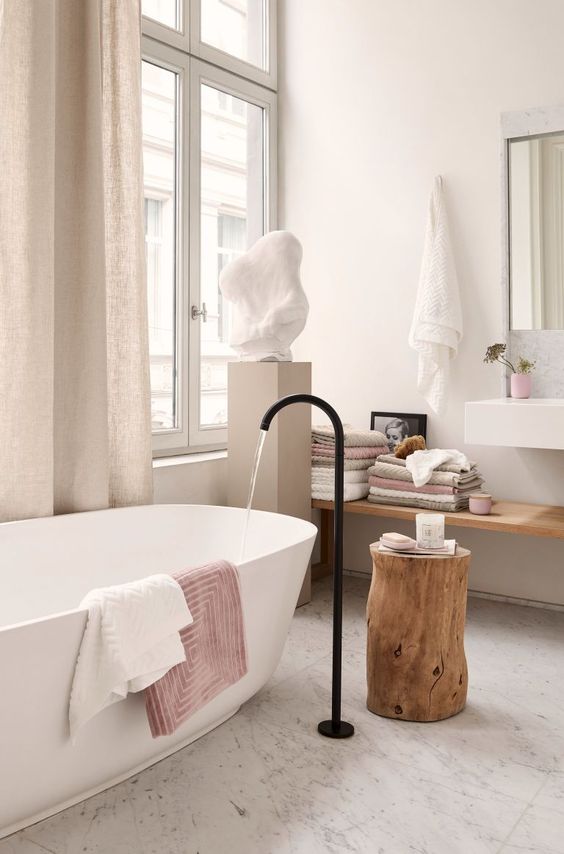 a lovely spa bathroom with an oval tub and a black faucet, a floating shelf, a wall mounted sink and a sculpture on a stand