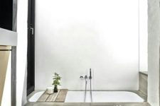 a minimalist bathroom done in concrete and with a white sunken bathtub is very simple, casual and with no fuss