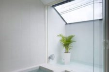 a minimalist bathroom with a skylight, a sunken bathtub, a shower space and a potted plant is clad with neutral tiles