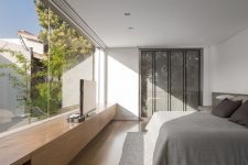 a minimalist bedroom with storage hidden in the wall, a bed, a sleek storage unit and a glass wall with a view of a private courtyard