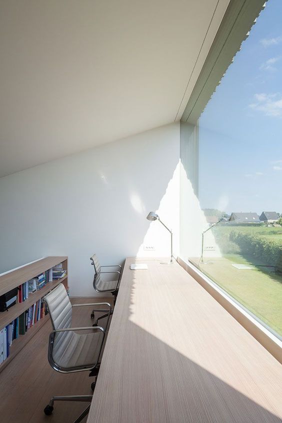 a minimalist home office with a glazed wall, a large and long sleek desk, a couple of chairs and a bookcase behind is perfect for working