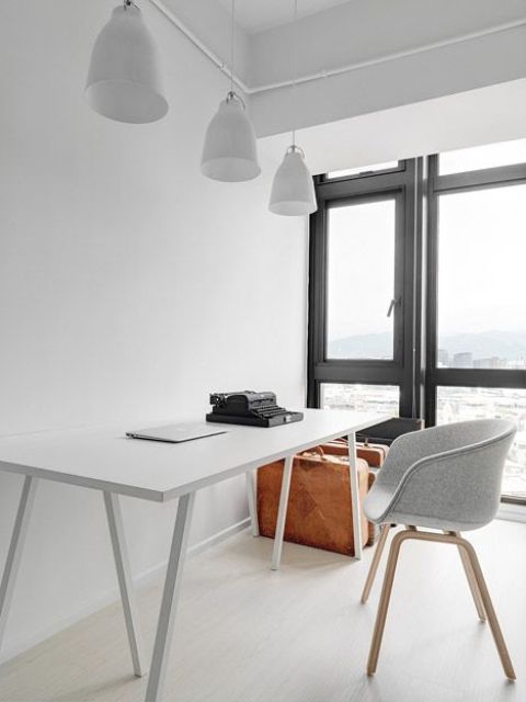 a minimalist home office with a glazed wall and a view of the city, a white desk, a grey chair and some storage units is cool