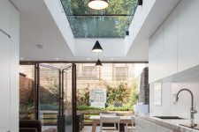 a minimalist kitchen with sleek white cabinets, a small dining space and a large skylight and a folding wall to enjoy a small provate garden