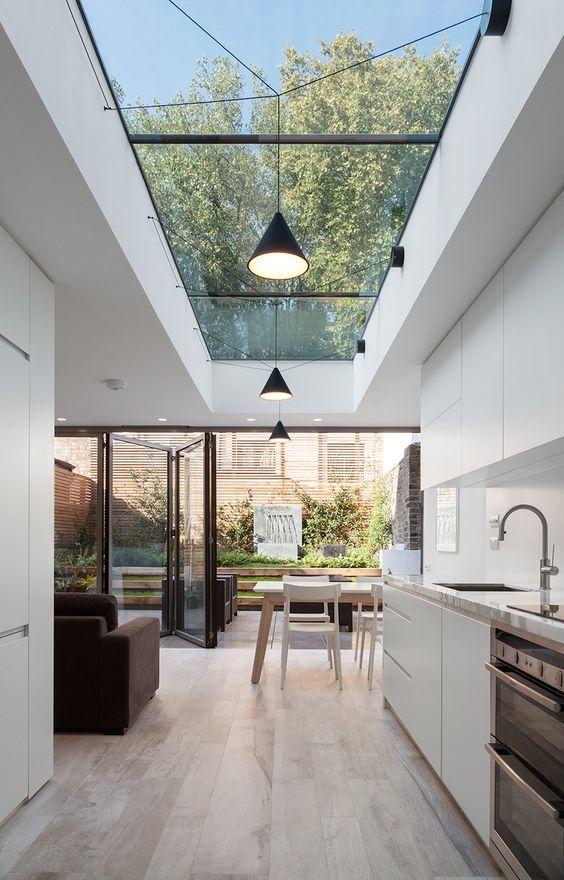 a minimalist kitchen with sleek white cabinets, a small dining space and a large skylight and a folding wall to enjoy a small provate garden