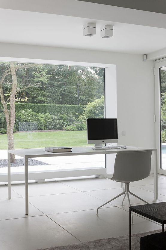 a minimalist white home office with large windows that let you enjoy the garden, a sleek white desk and a chair is a lovely space to work in