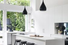 a minimalist white kitchen with sleek cabinets, white stone countertops, black pendant lamps and a glazed wall that looks on the garden